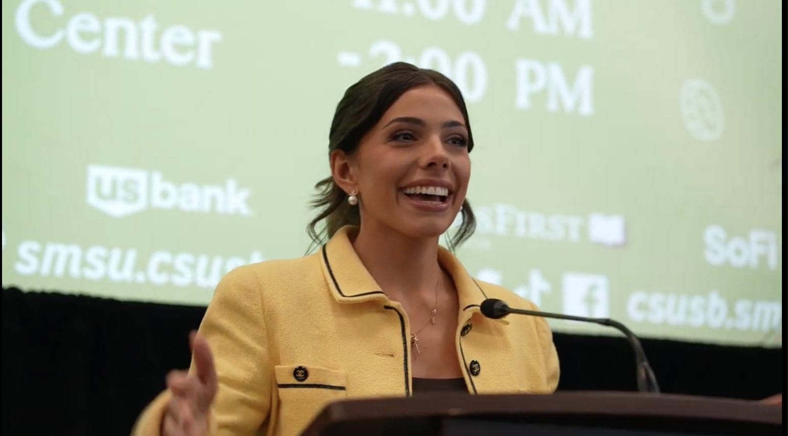 Close-up of Taylor Price speaking at the podium at California State University, San Bernardino, with the Financial Literacy Summit screen behind her.